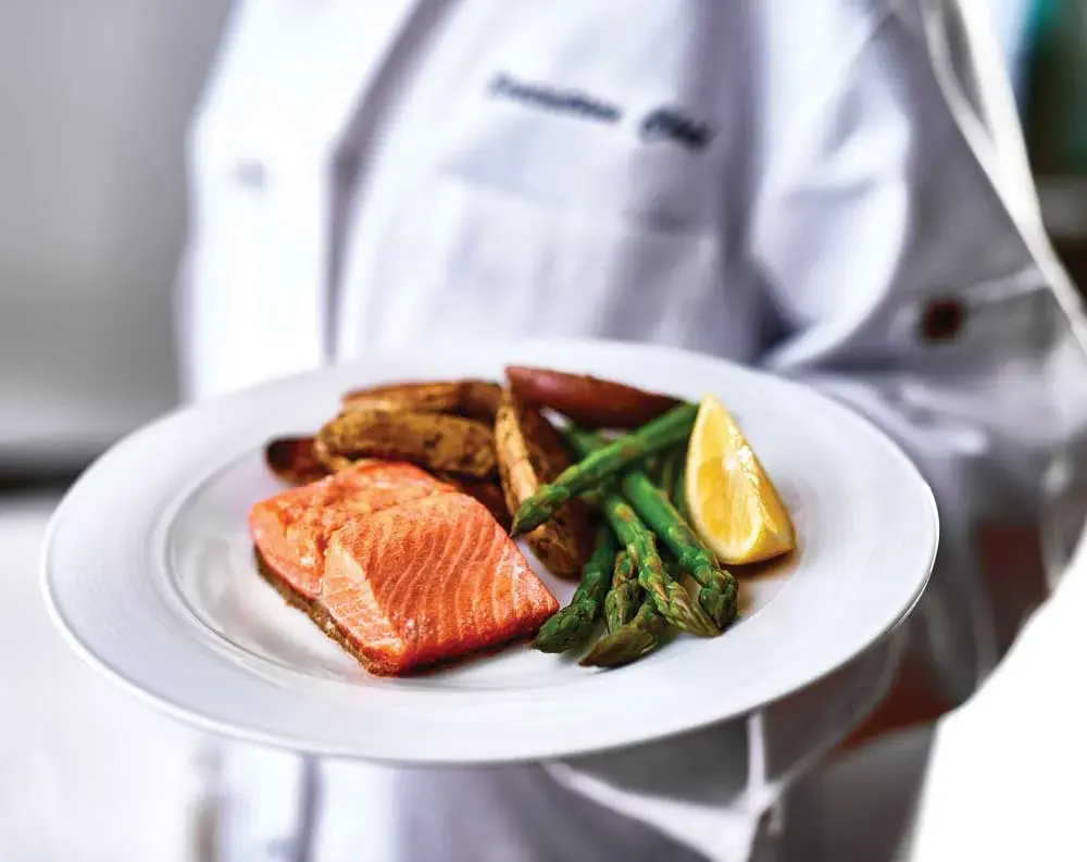 [[community_name]] Chef Created Meals, chef delivering a finished dish.